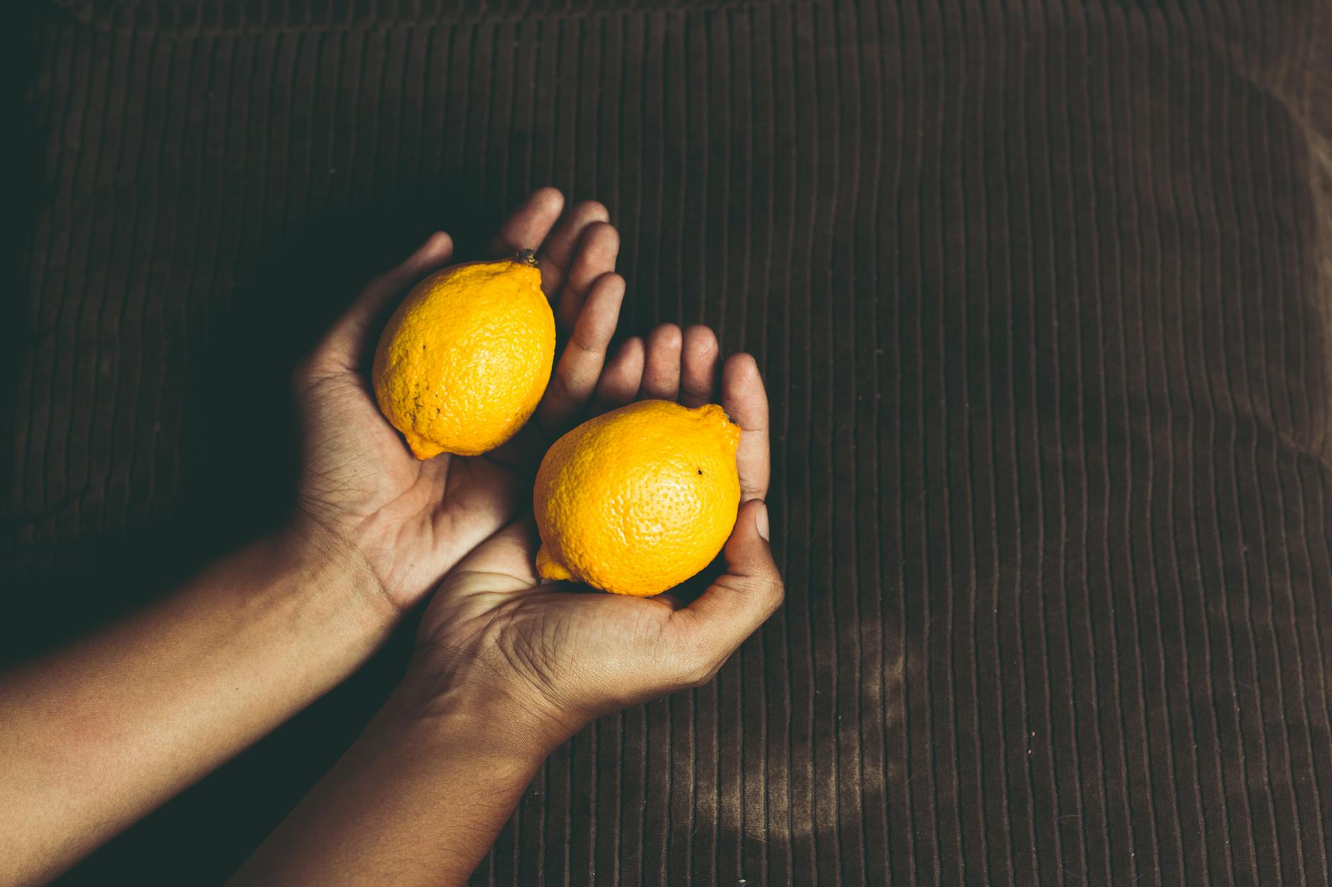 Due limoni freschi tenuti in mani a coppa su una superficie marrone, simbolo di freschezza e vitalità.