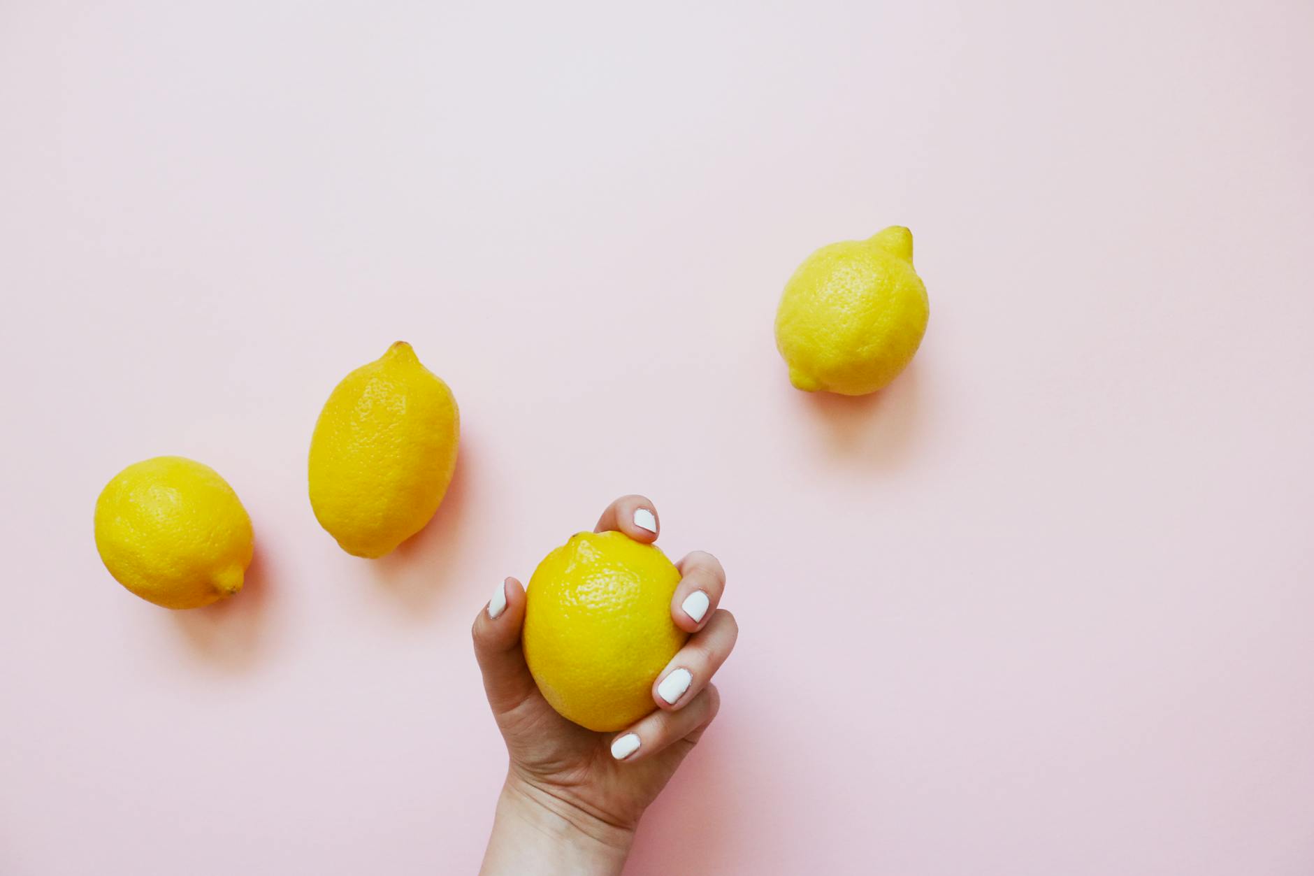 Hand holding a fresh lemon on soft pink background with citrus fruits