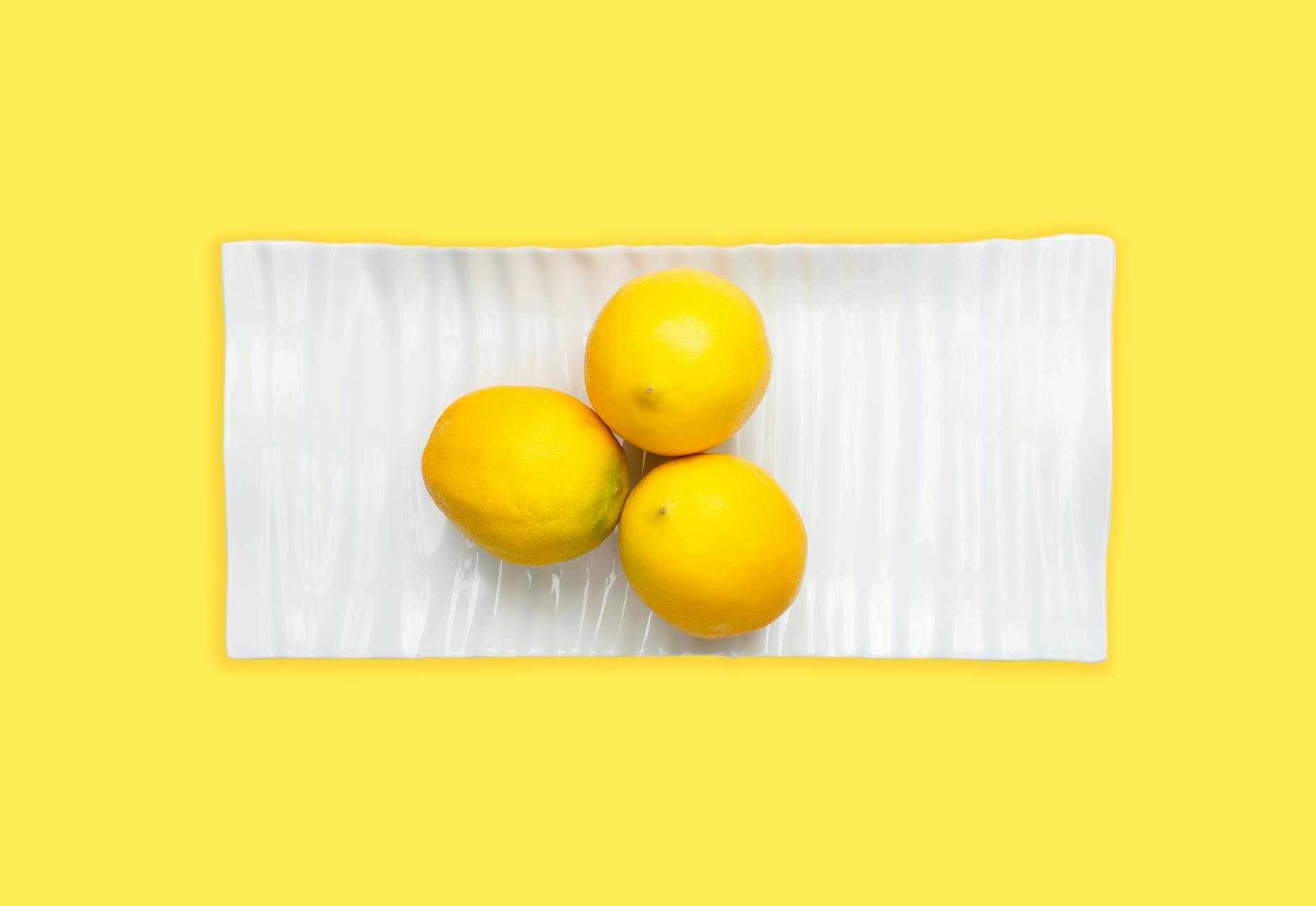 Fresh lemons on white plate with yellow background, symbolizing brightness and renewal