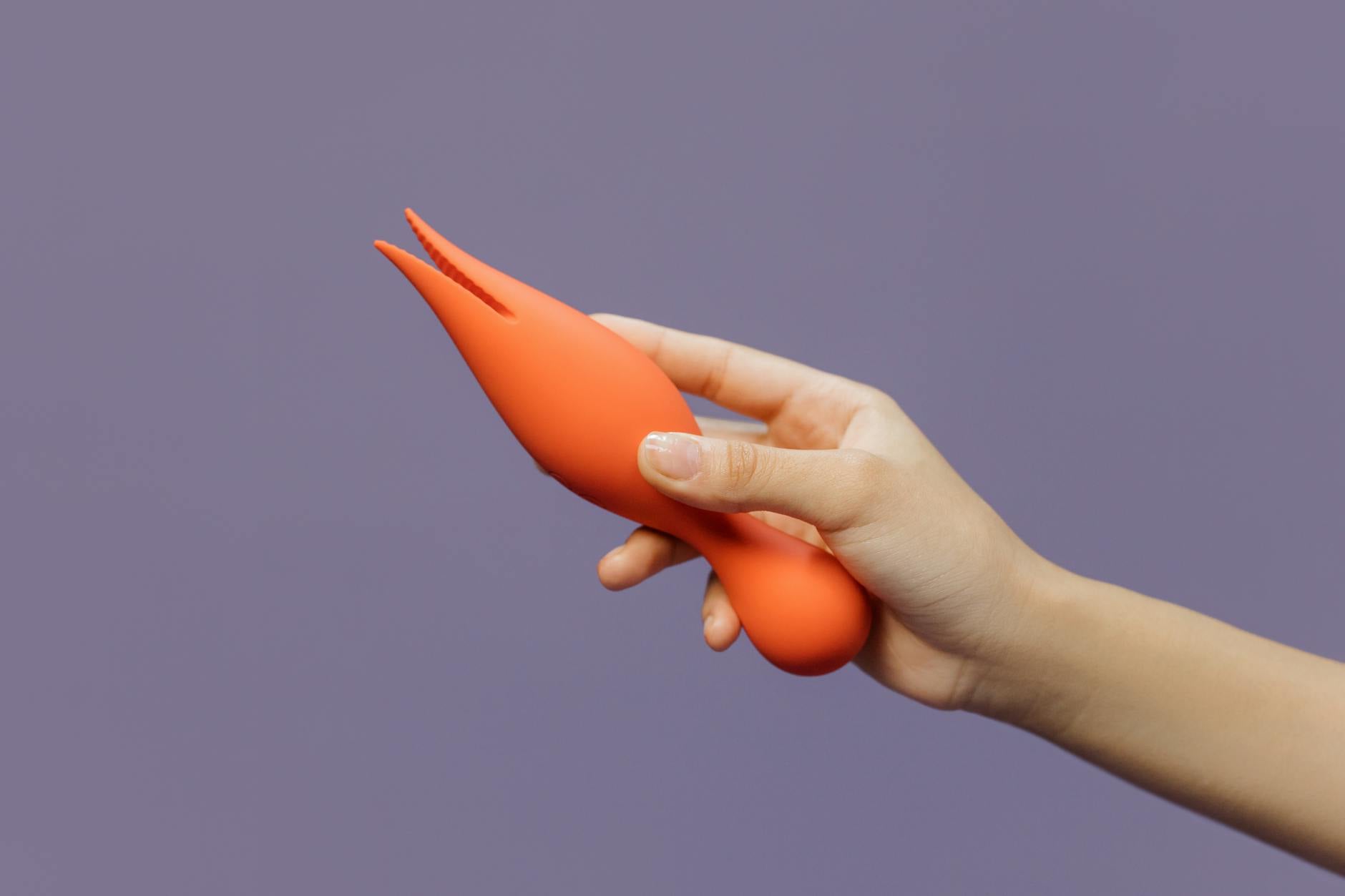 Hand holding a vibrator against a minimalistic purple backdrop