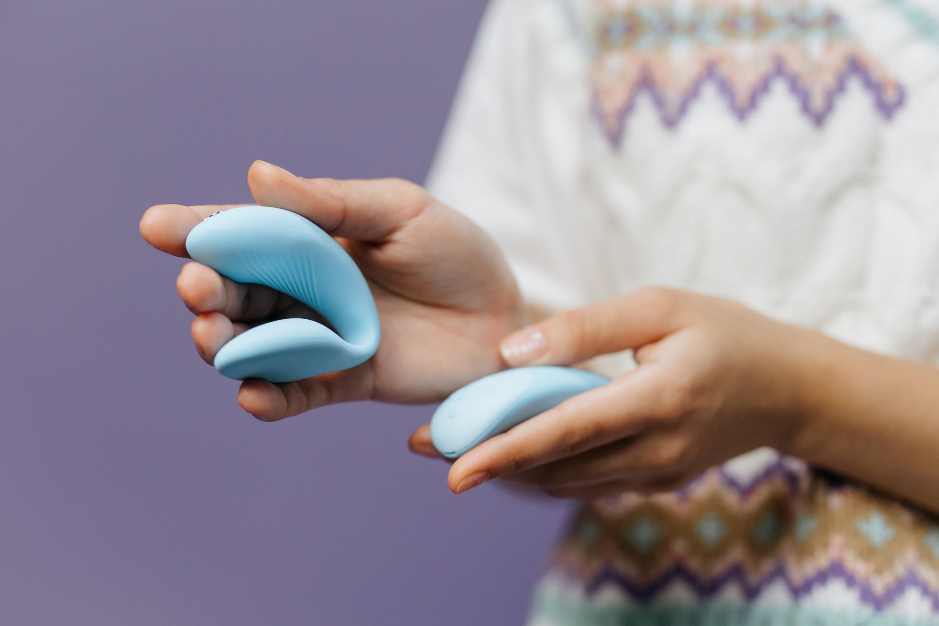 Close-up of hands holding a sleek blue clitoral vibrator with intention and openness.