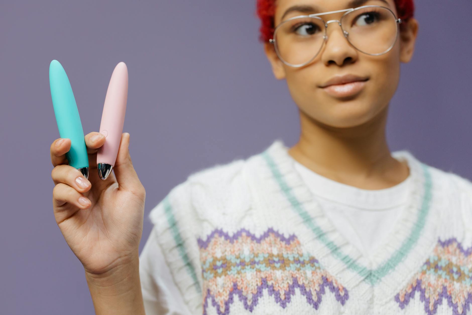 A young woman holds colorful vibrators against a purple background, representing diverse options for beginners exploring lemon vibrators.