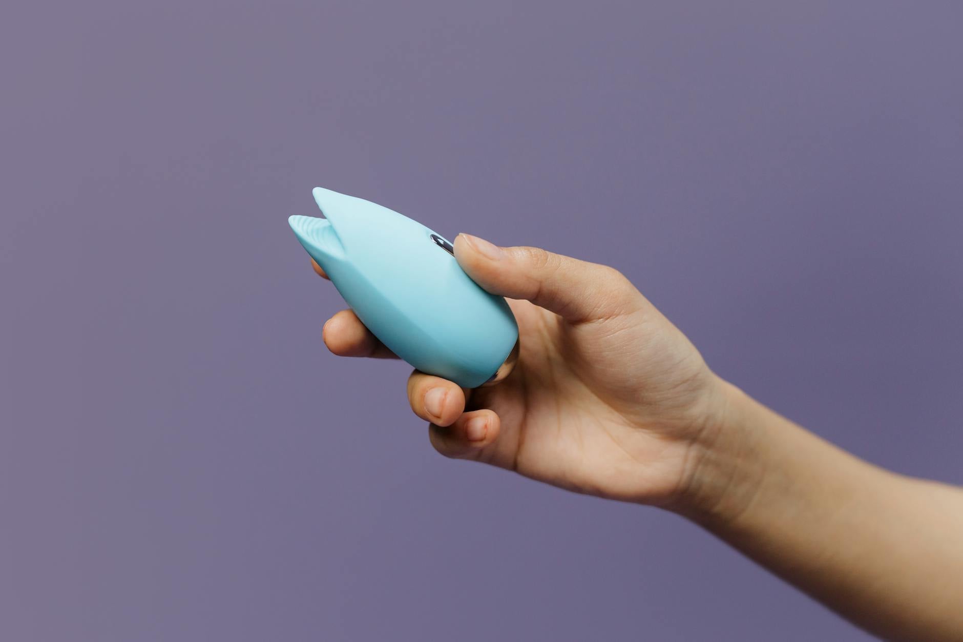 Un vibratore colorato tenuto in mano su sfondo lilla, che simbolizza il piacere consenziente e l'esplorazione intima.