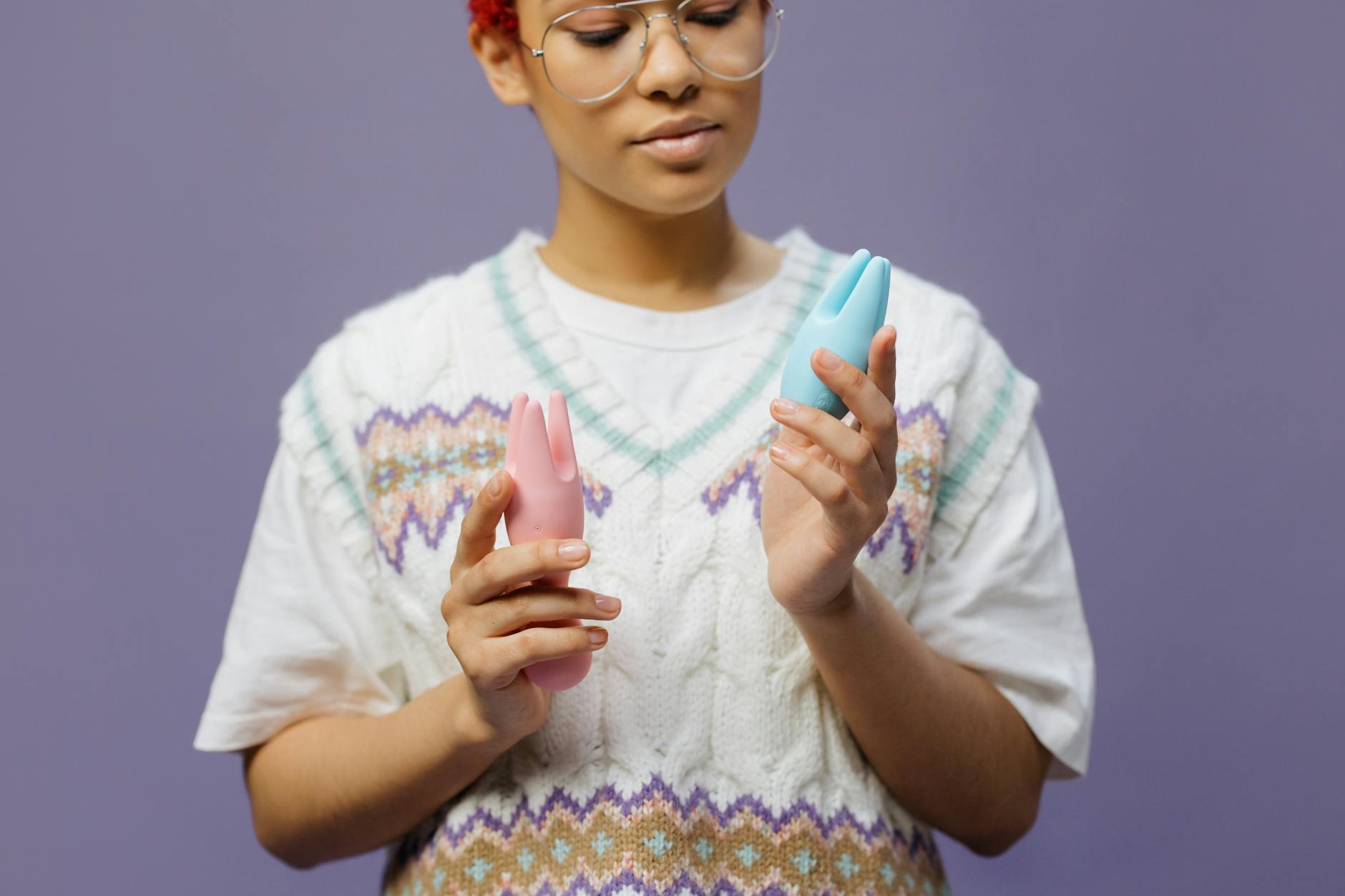 Woman holding blue and pink clitoral vibrators in a thoughtful pose