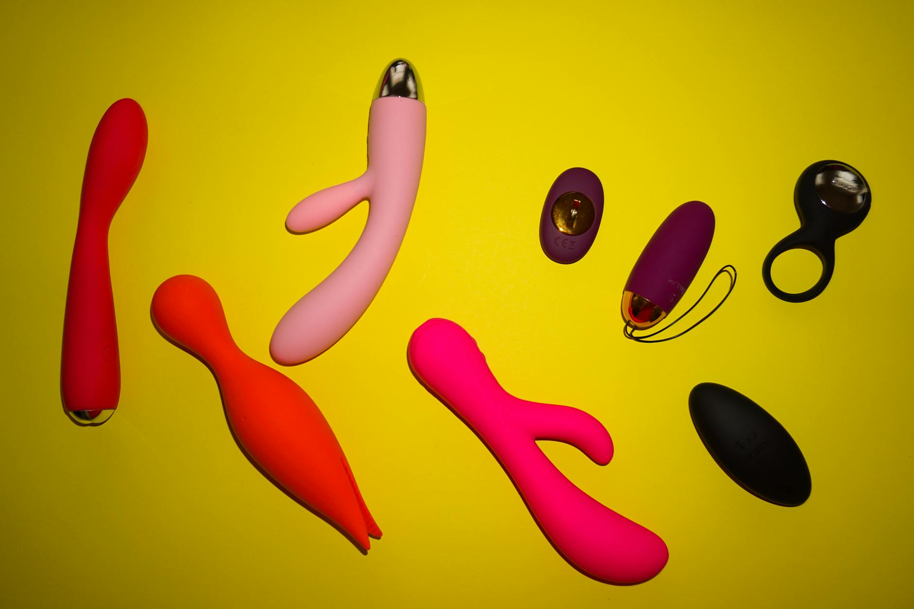 Colorful collection of body-safe vibrators and toys displayed on a bright yellow surface