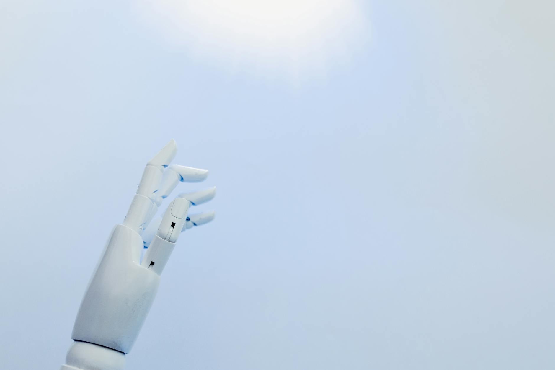 A robotic hand reaching towards a bright light on a white background symbolizing innovation.