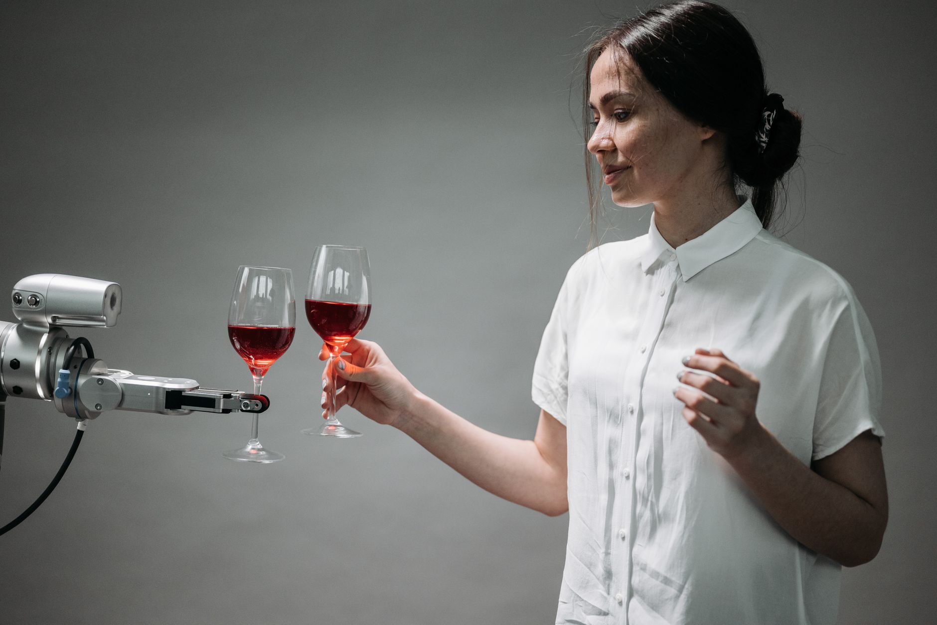 A woman and robotic hand clink glasses of red wine together
